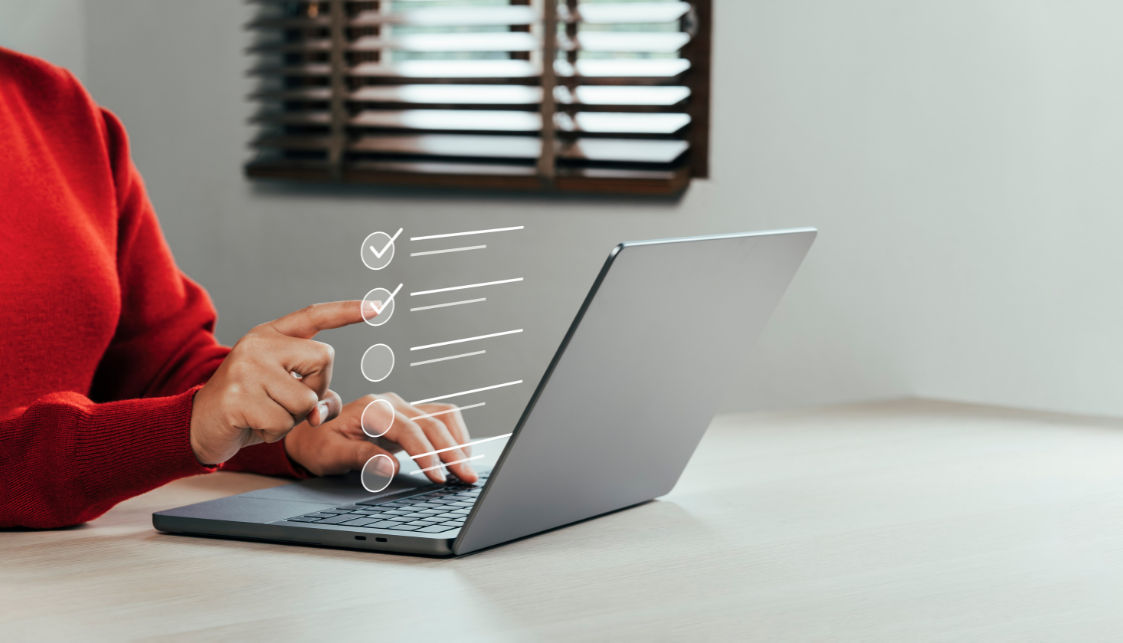 A person whose arm can only be seen selects virtual items from a list in front of a laptop placed on a table.