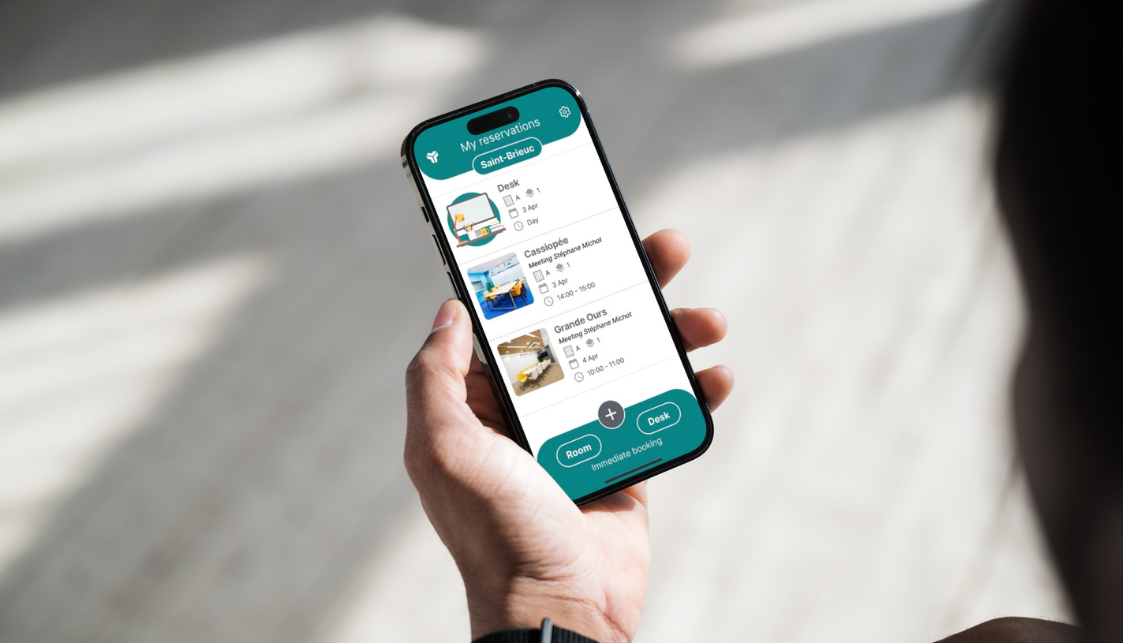 A smartphone in one hand with a list of room and office reservations on the screen.